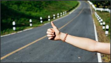 Illustration 560x315 rawpixel 250917 unsplash a person hitchhiking holding out hand with thumbs up in front of a road